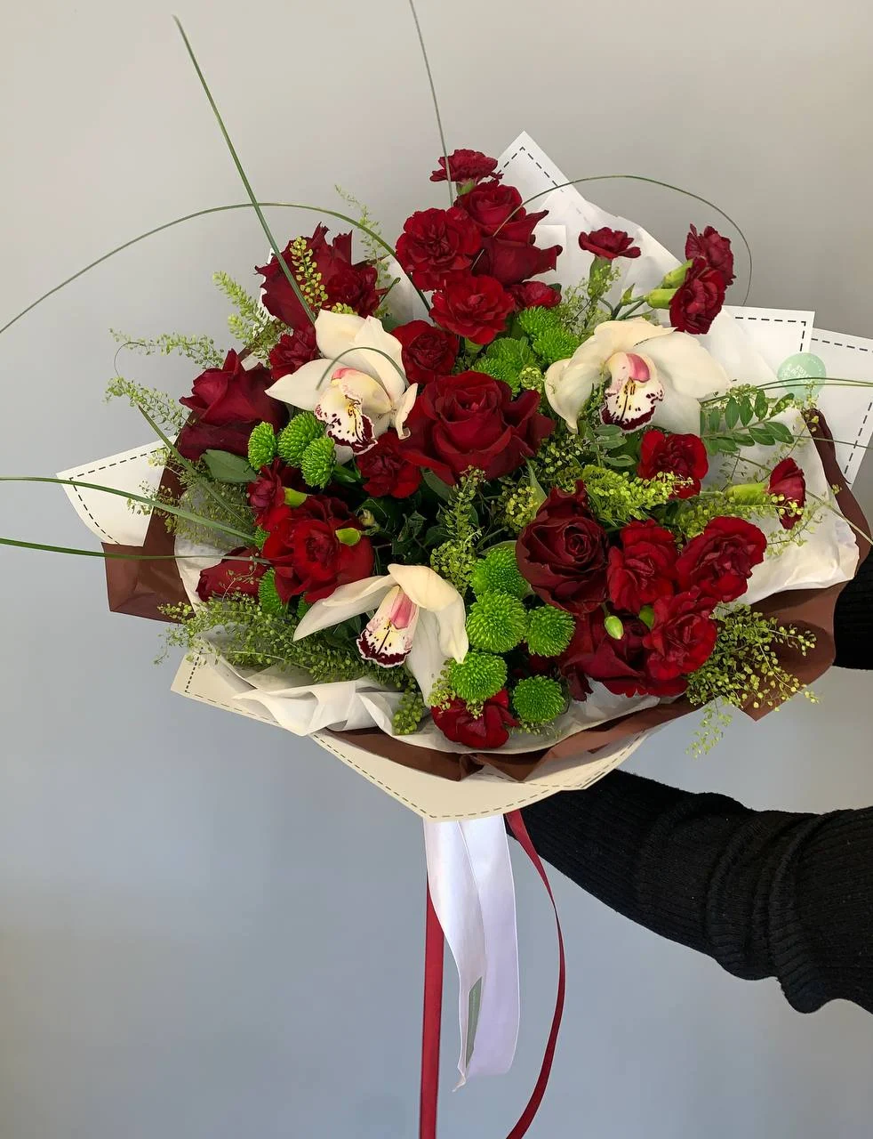 Okazały bukiet różami, orchideami i zielonymi kwiatami w białym papierze