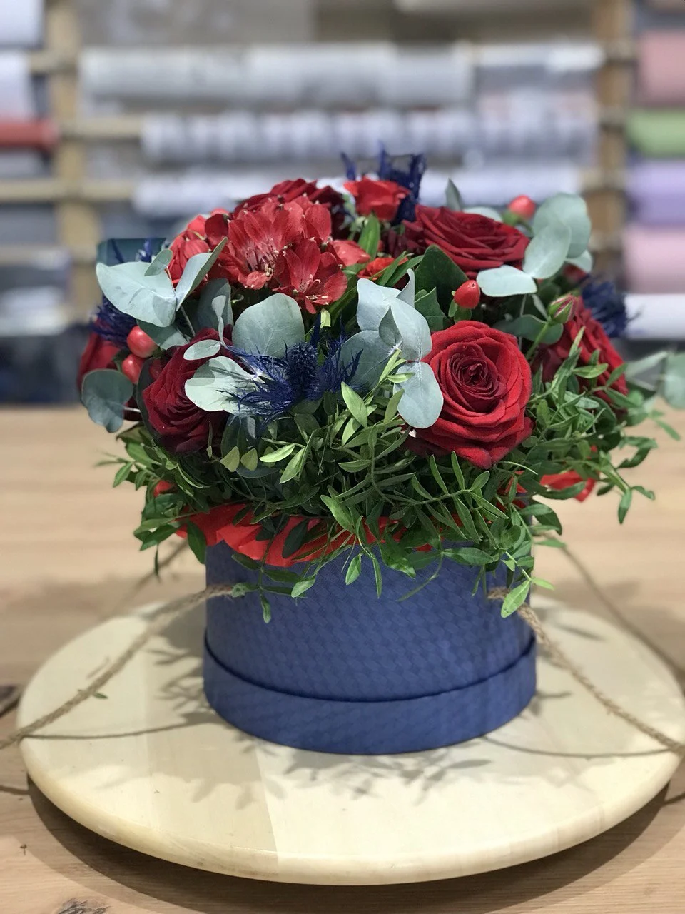 Flower box z czerwonymi różami, niebieskimi ostami, eukaliptusem i zielenią dekoracyjną w granatowym pudełku