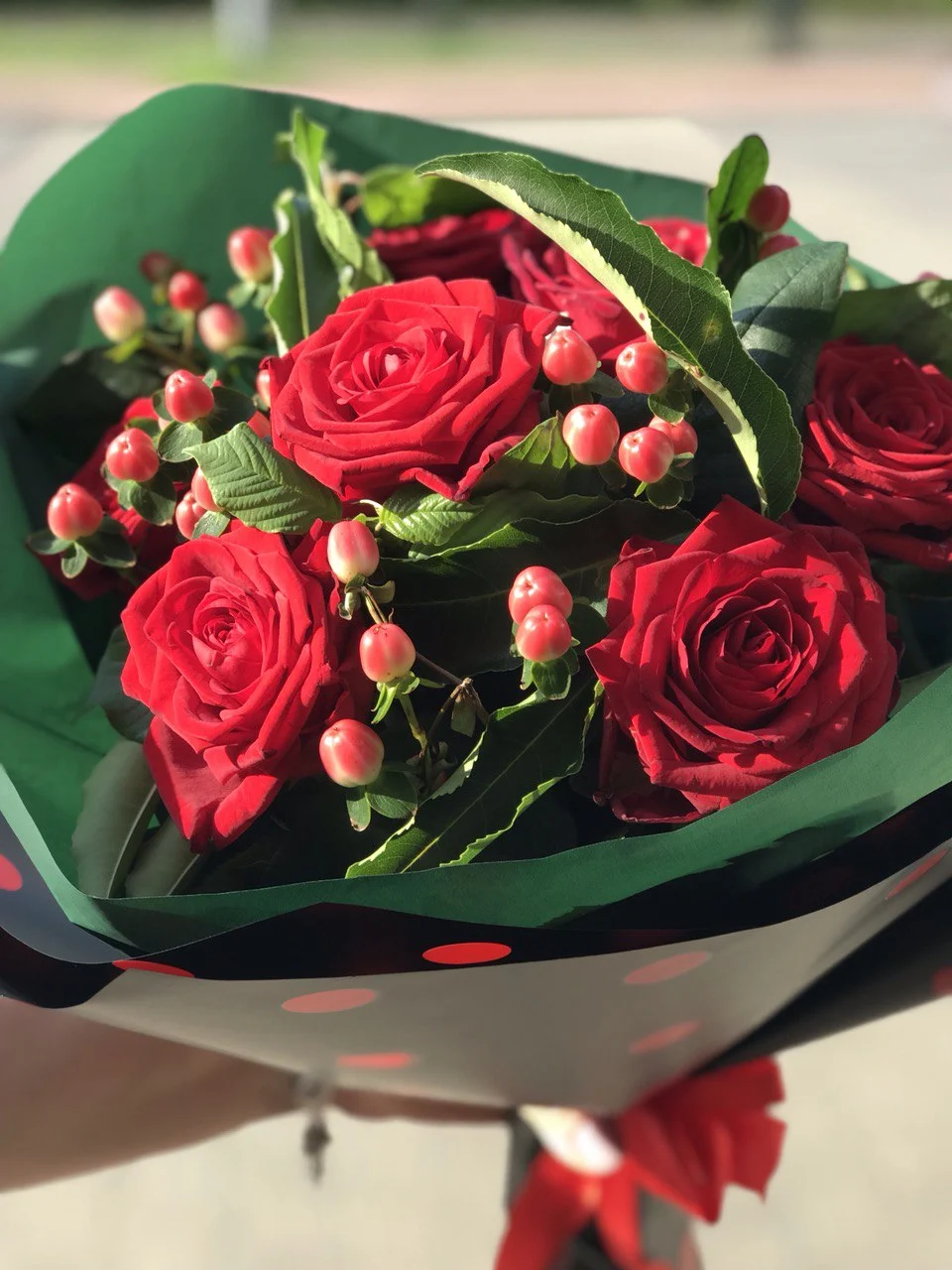 Bukiet róż z czerwonymi jagodami w zielonym papierze