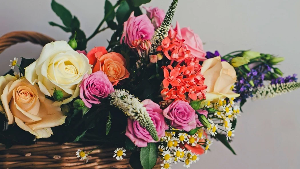 Kolorowy bukiet kwiatów w koszu – róże, stokrotki i inne kwiaty mieszane