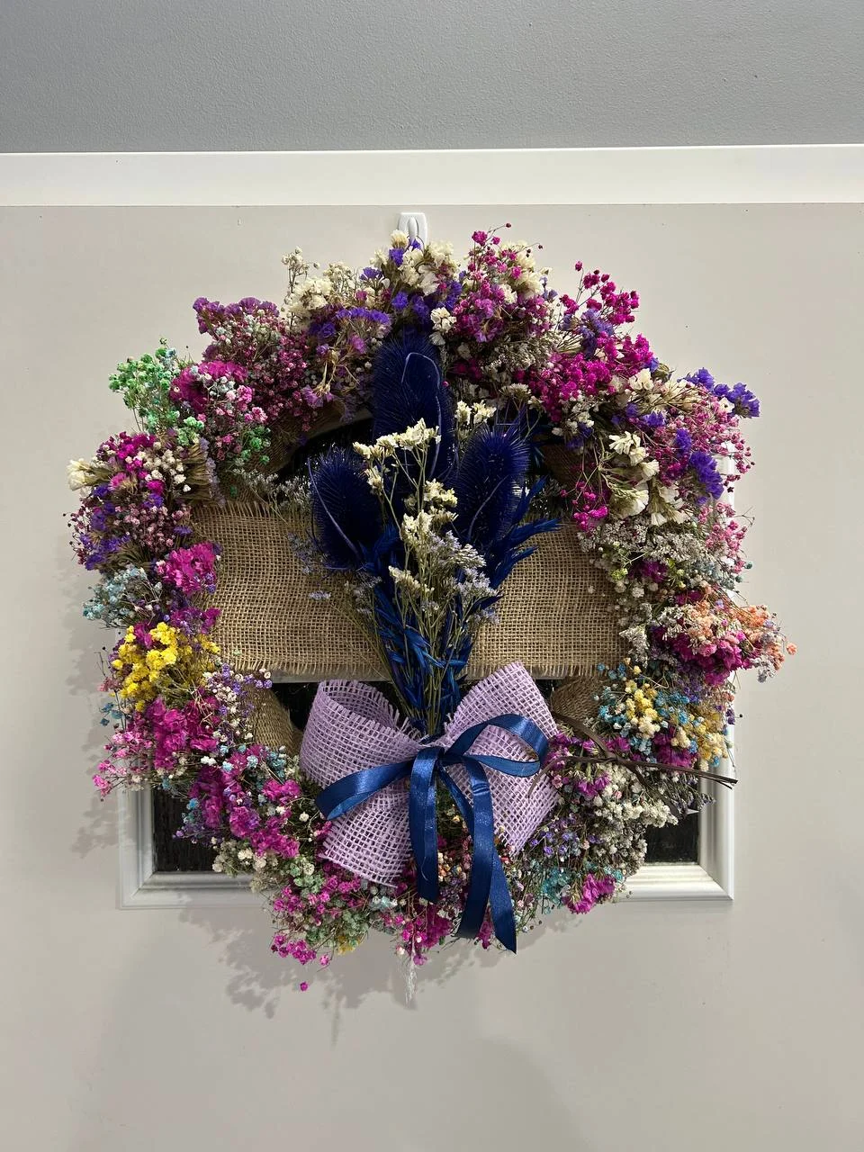 Dekoracja z kolorowej gipsówki i suszonych kwiatów z niebieską wstążką – barwny wieniec na drzwi