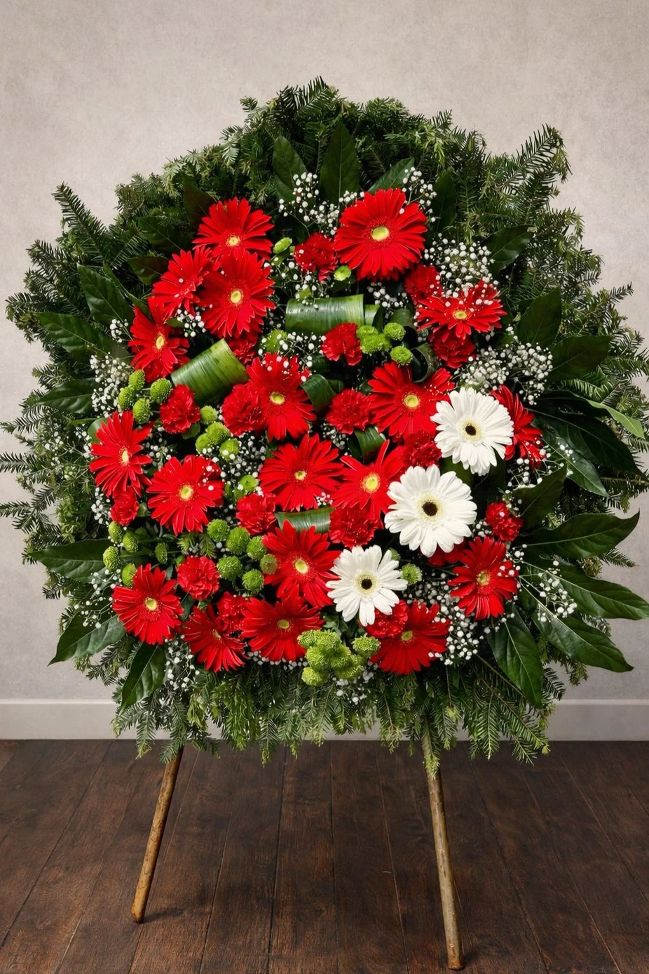 Wieniec pogrzebowy z gerberami i czerwonymi goździkami na stojaku